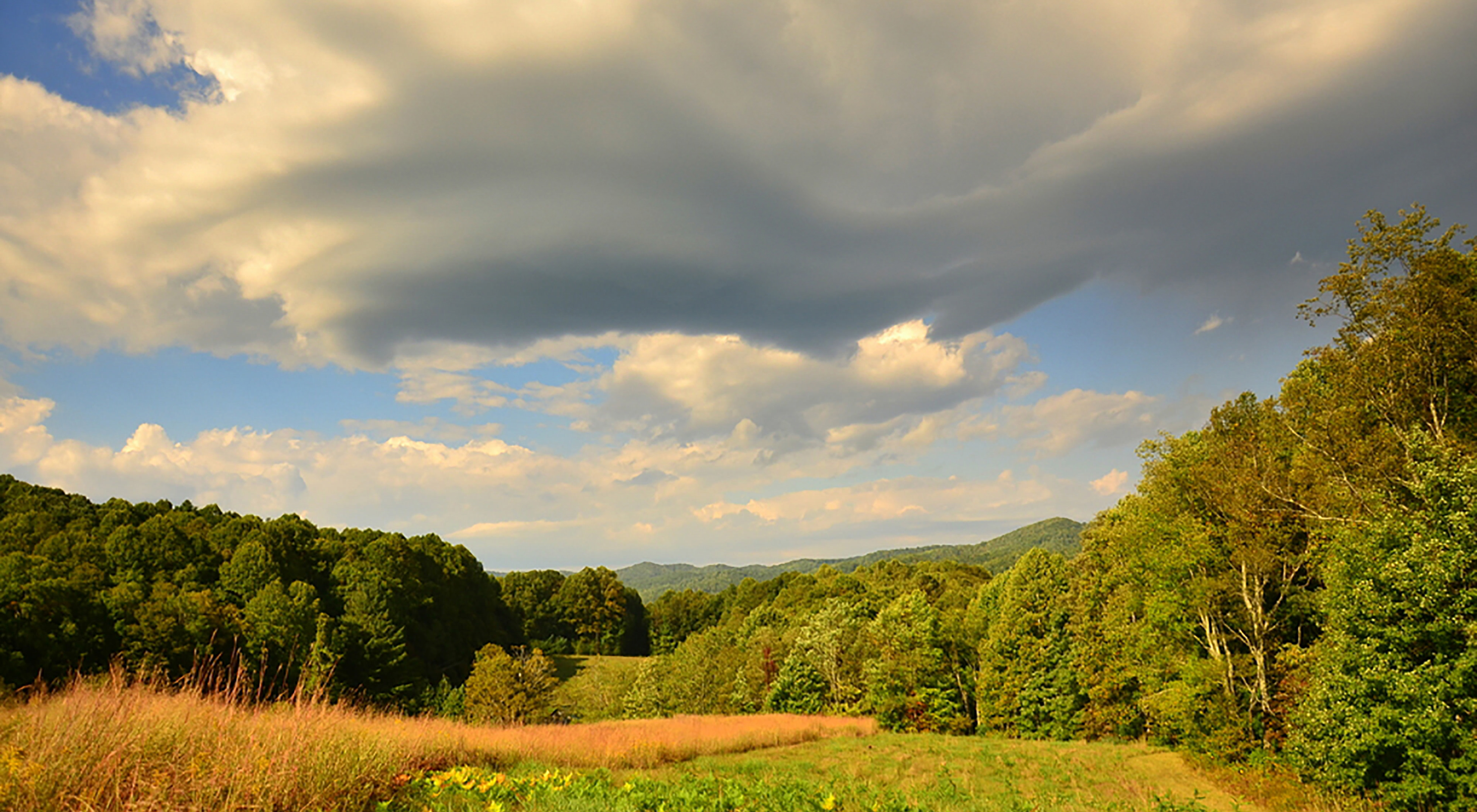 Thick, white clouds float over a green mountain valley.