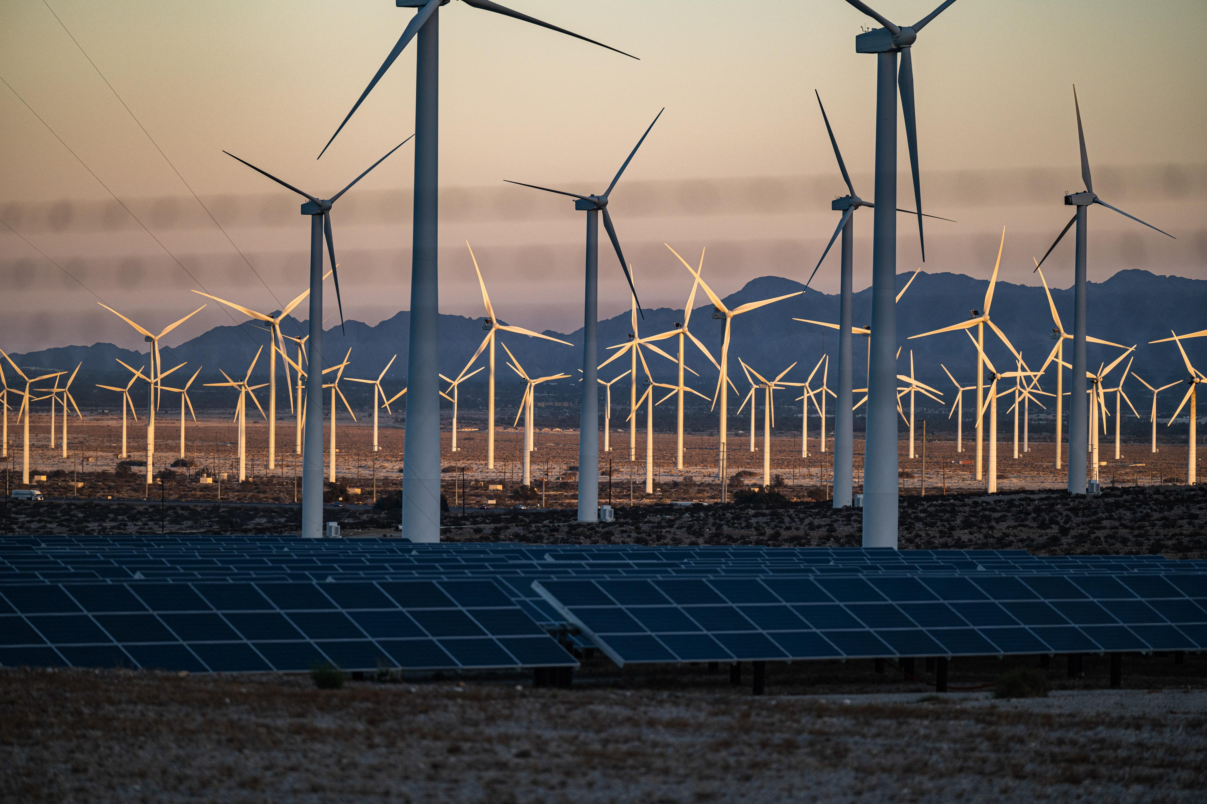 Solar panels and wind turbines in front of mountains. 