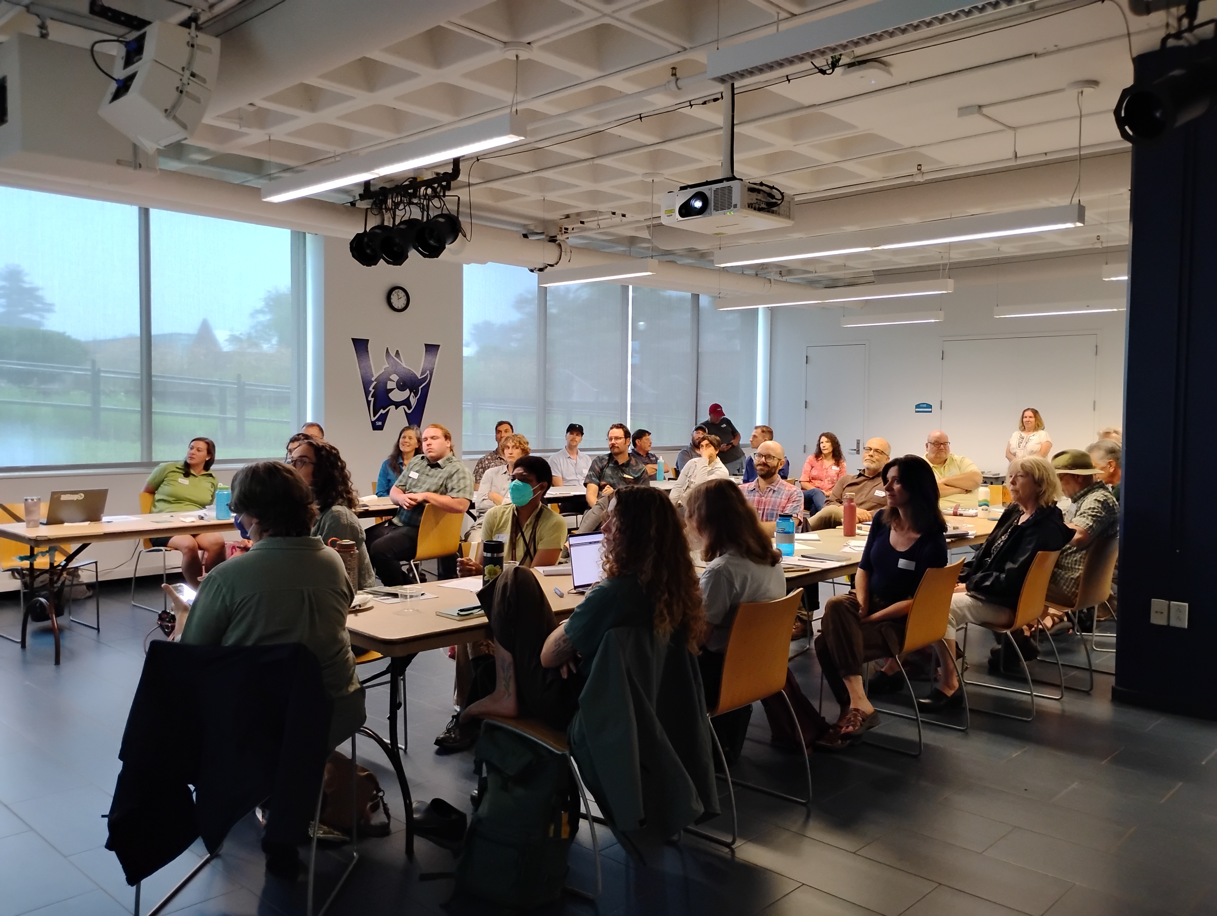 A group of people gather around a 'U' shaped desk set-up for a meeting.