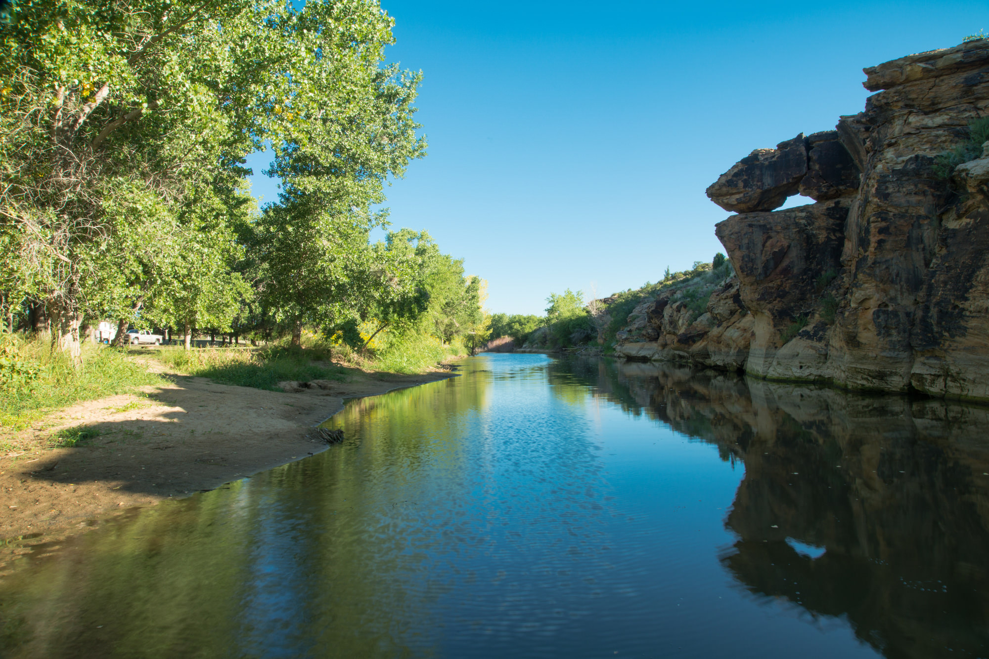 A creek bordered on either side by rock formations and native trees.
