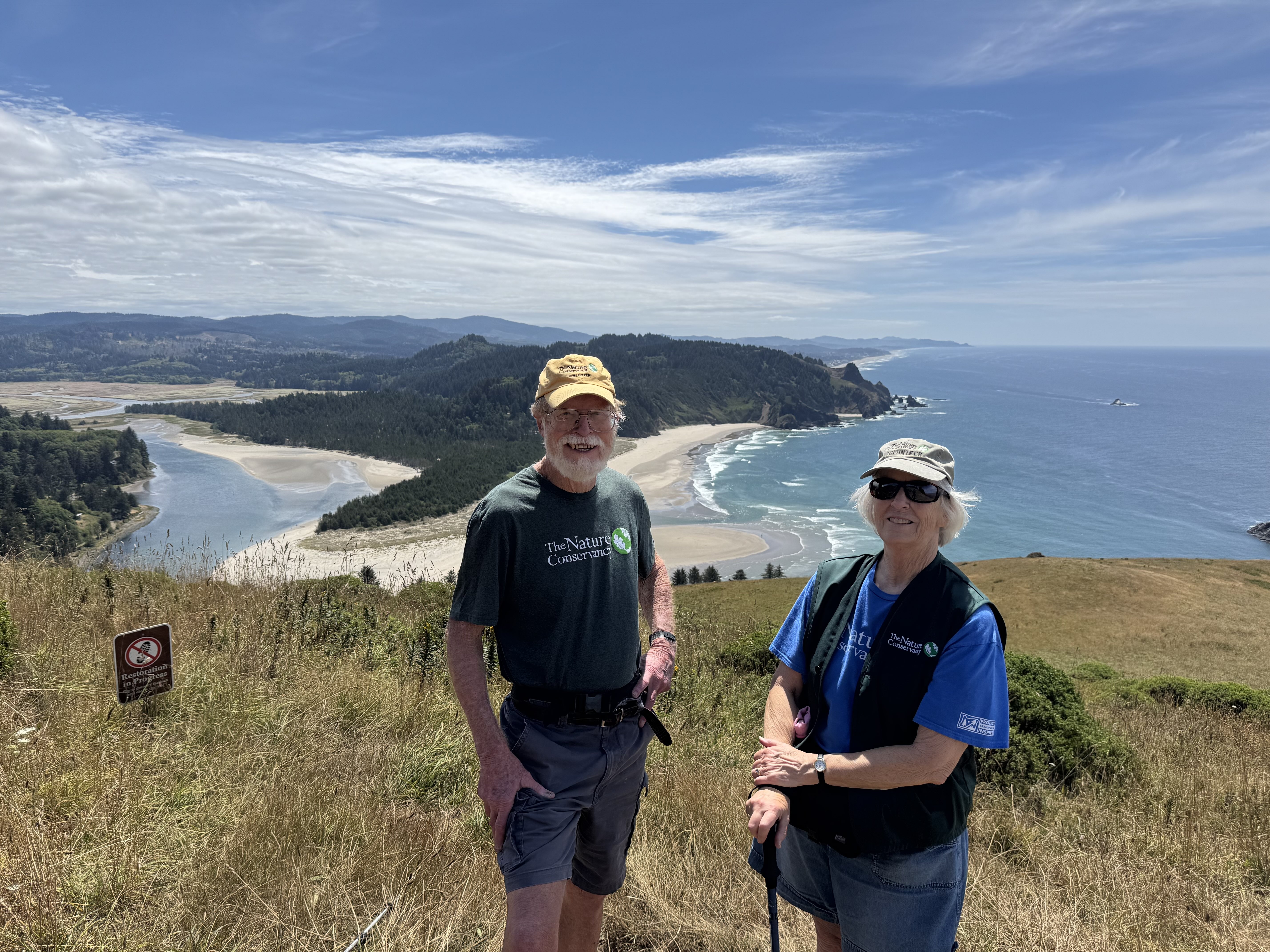 Two people stand on a cliff overlooking the ocean.