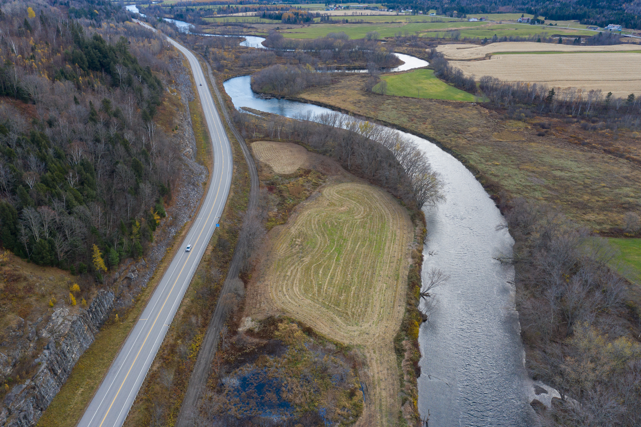 A river winds through farmland. A road parallels it to the left.