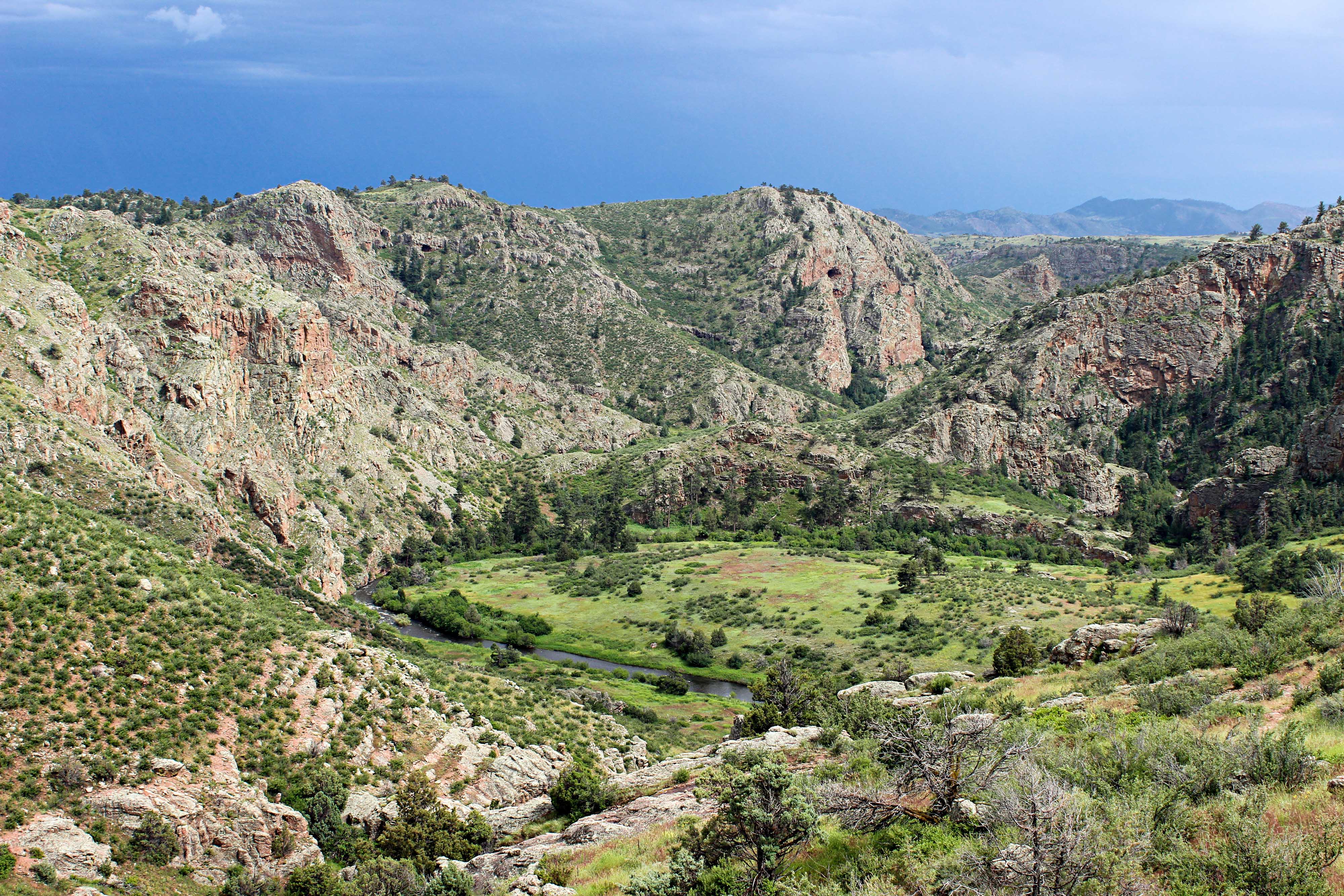 Aerial view looking down into Phantom Canyon in Colorado, showing a green valley with a stream running through it surrounded by high, rocky mountains.