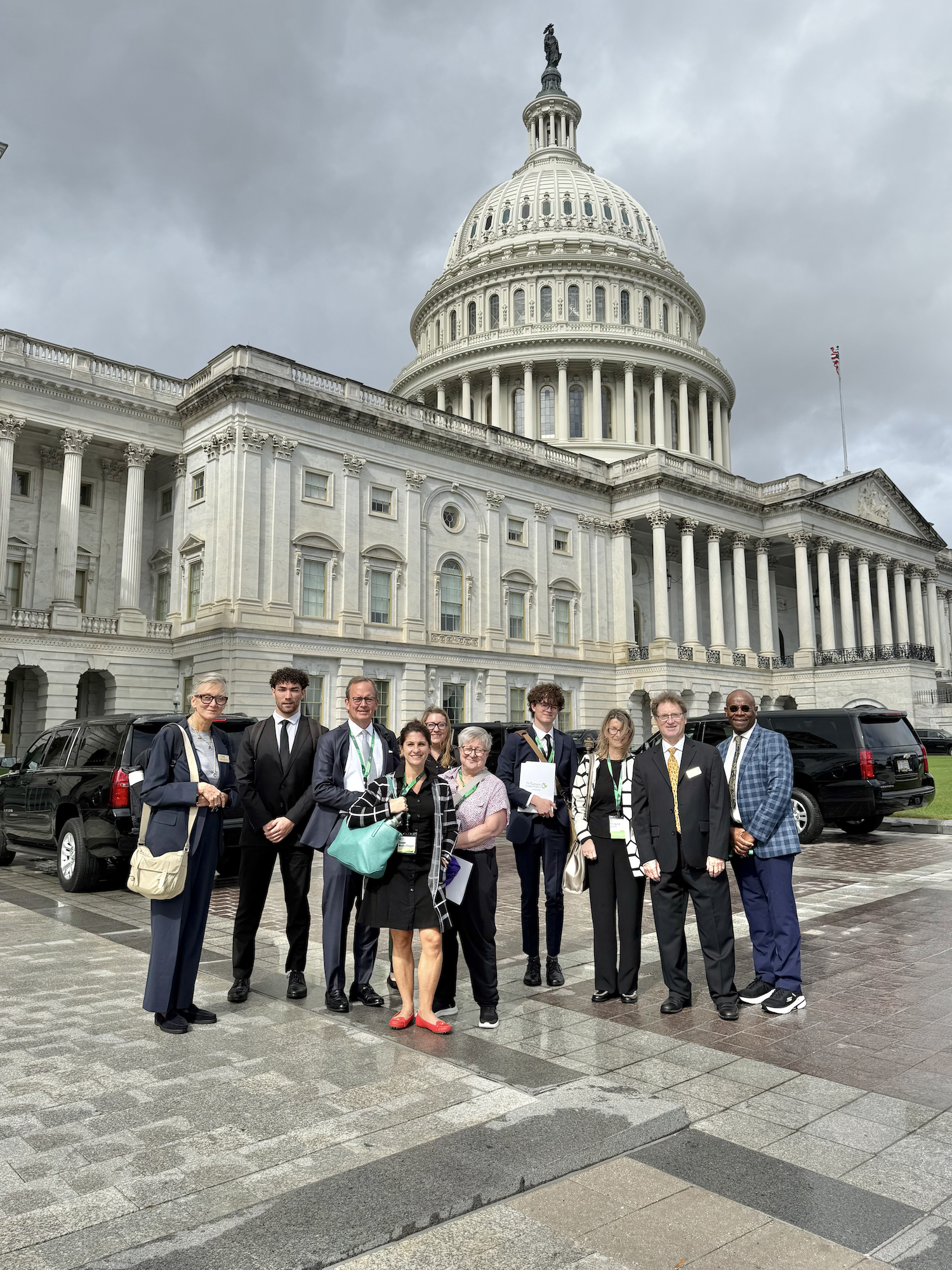 A group of people standing in front of the United States Capitol Building under an overcast sky.