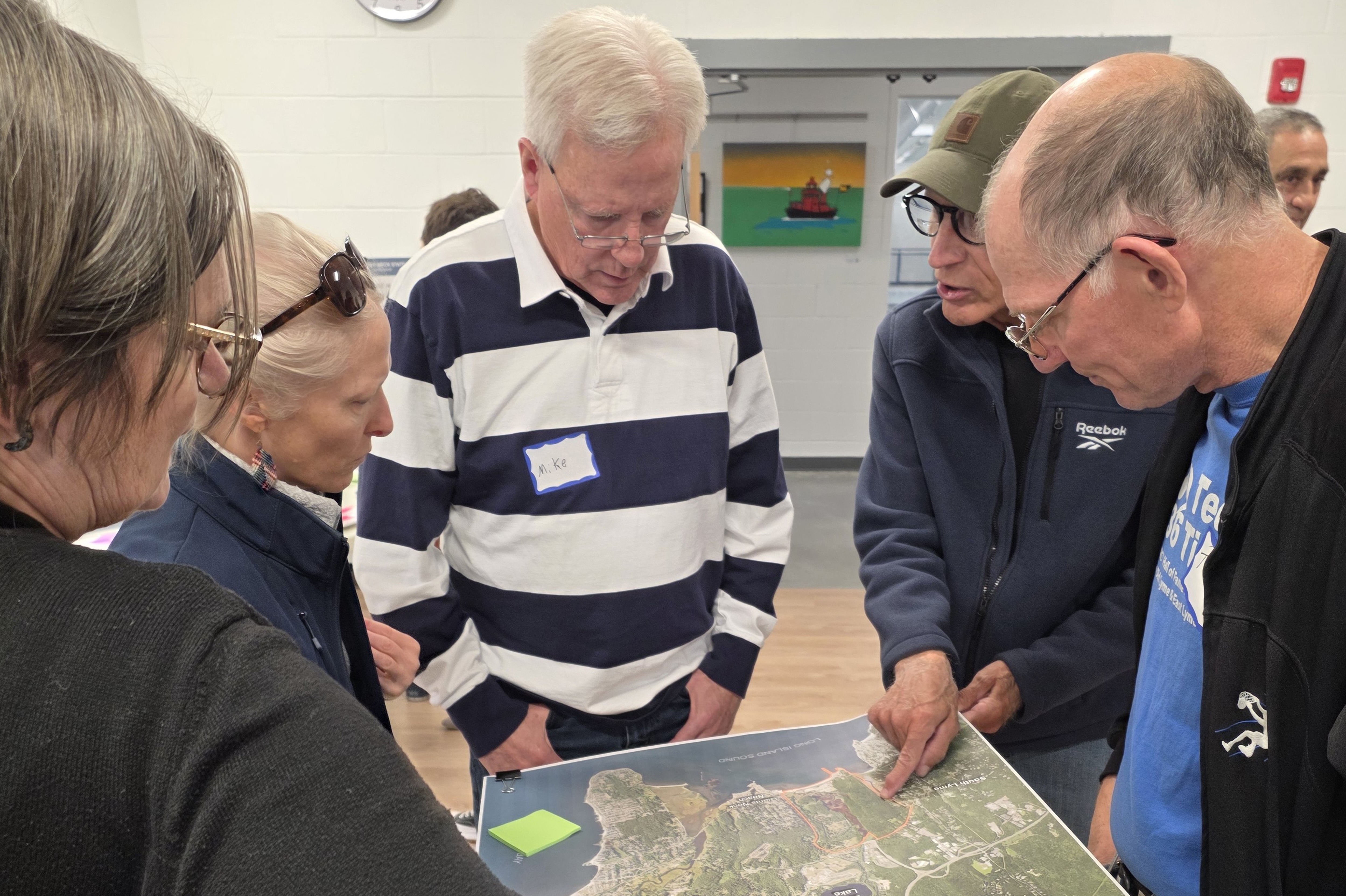 Group of adults examining a large map held out, focusing intently on specific details during a community meeting.