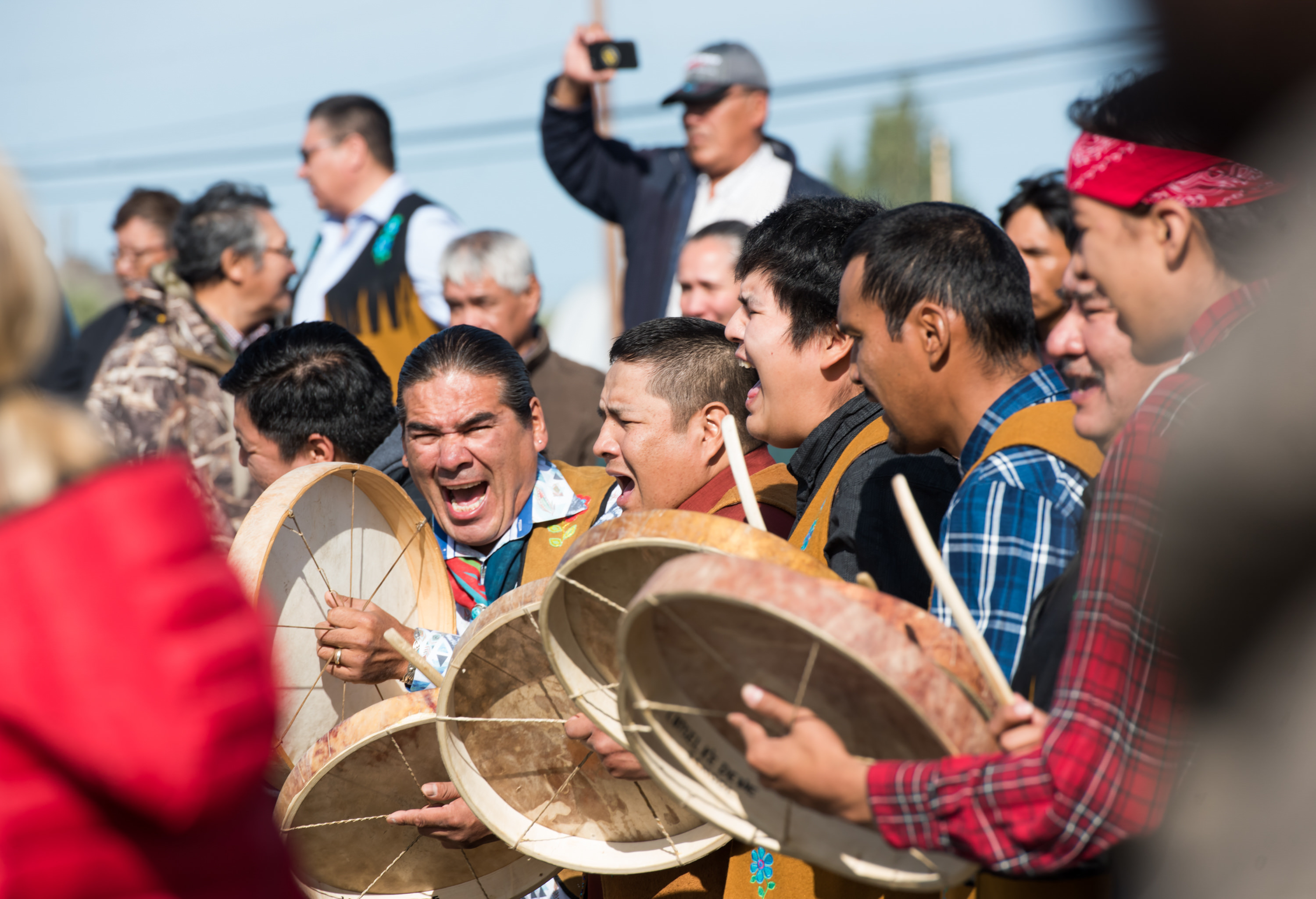 A group of men stand together and bang drums and yell.