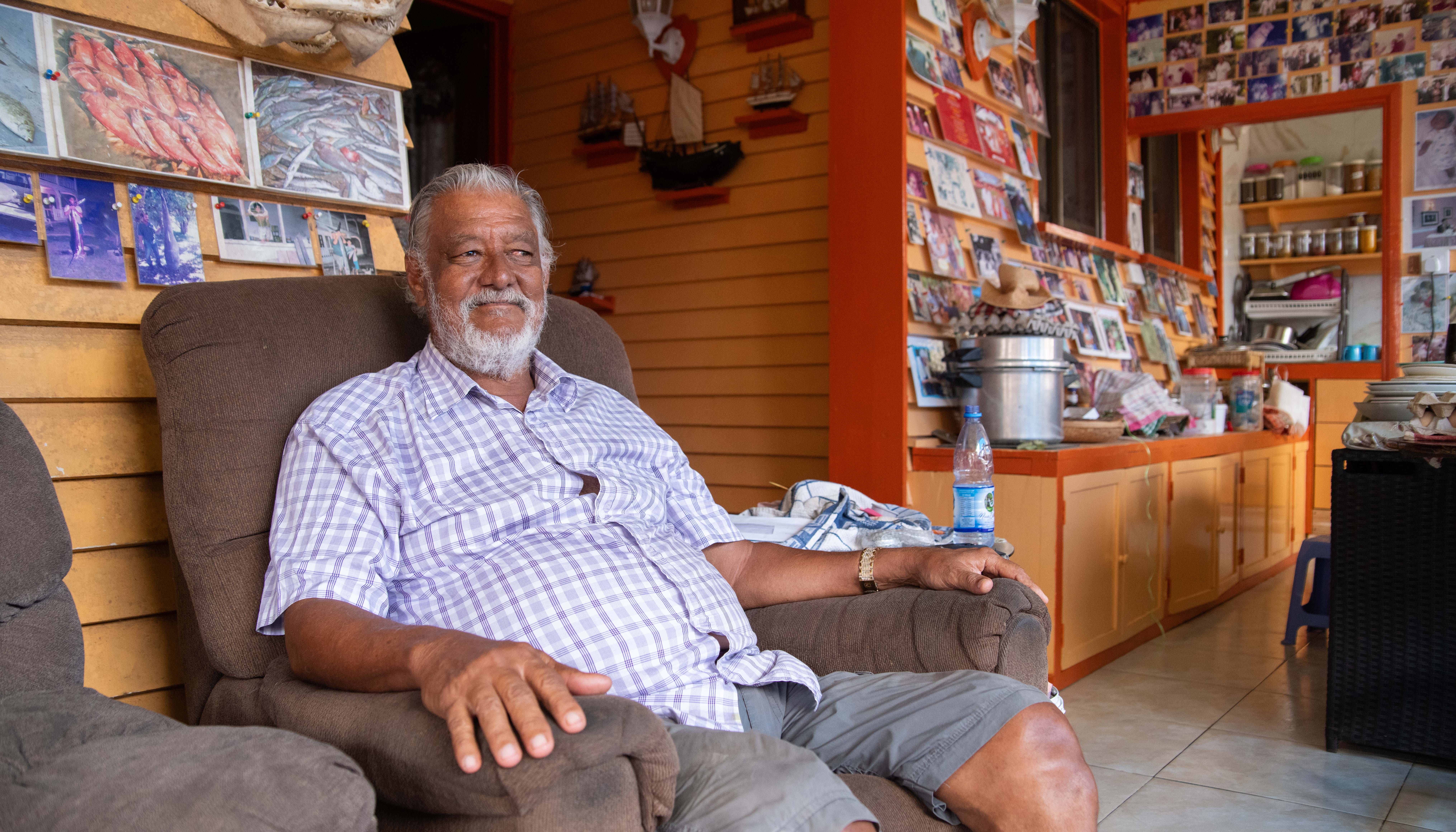 Man smiles as he sits on armchair, books behind him.