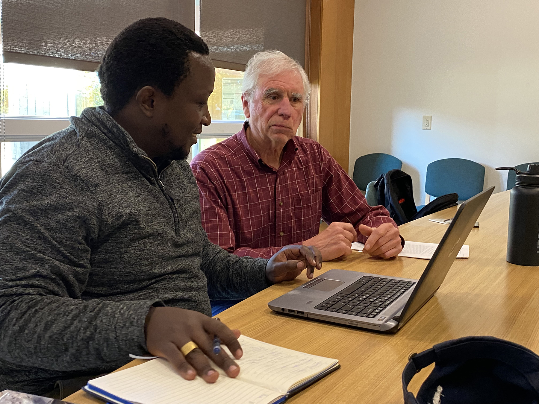 Edwin Njuguna and Dave Courtemanch sit at a table with a laptop.