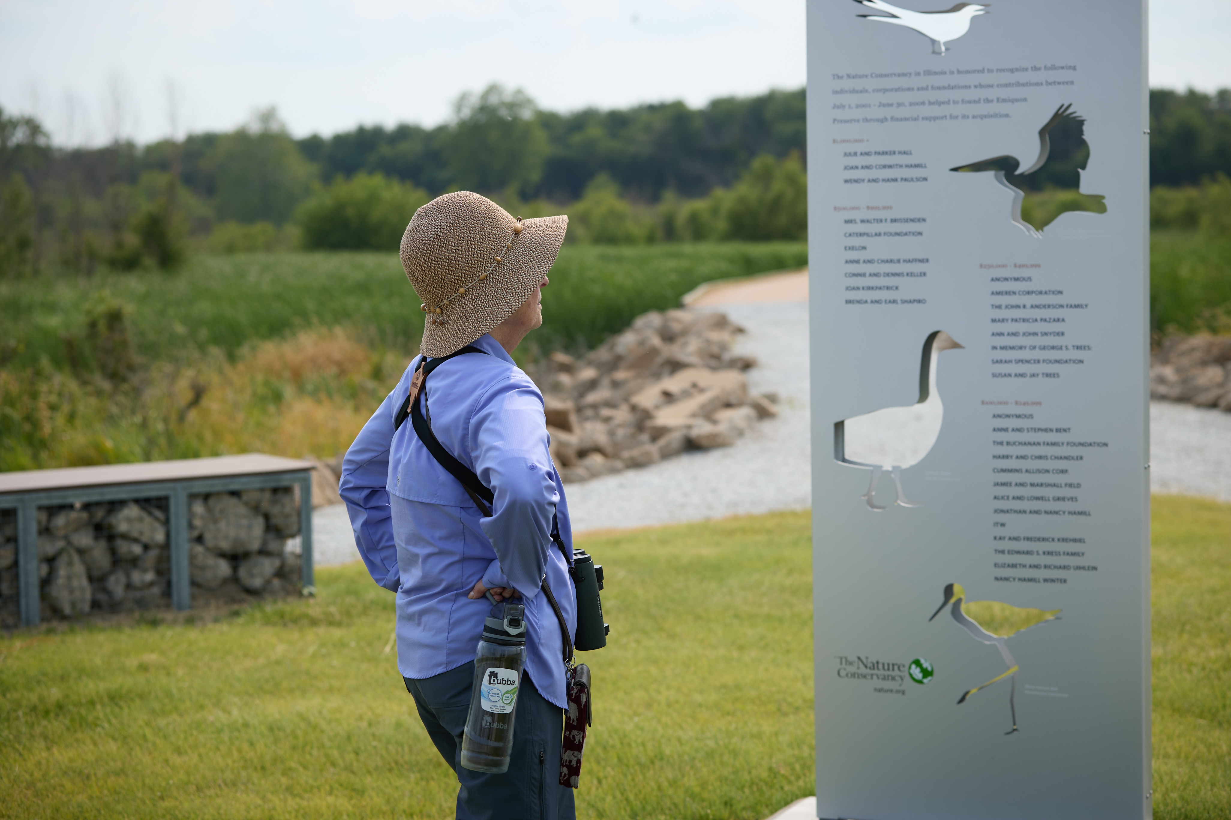 A person in a bucket hat looks at a sign at Emiquon Preserve.