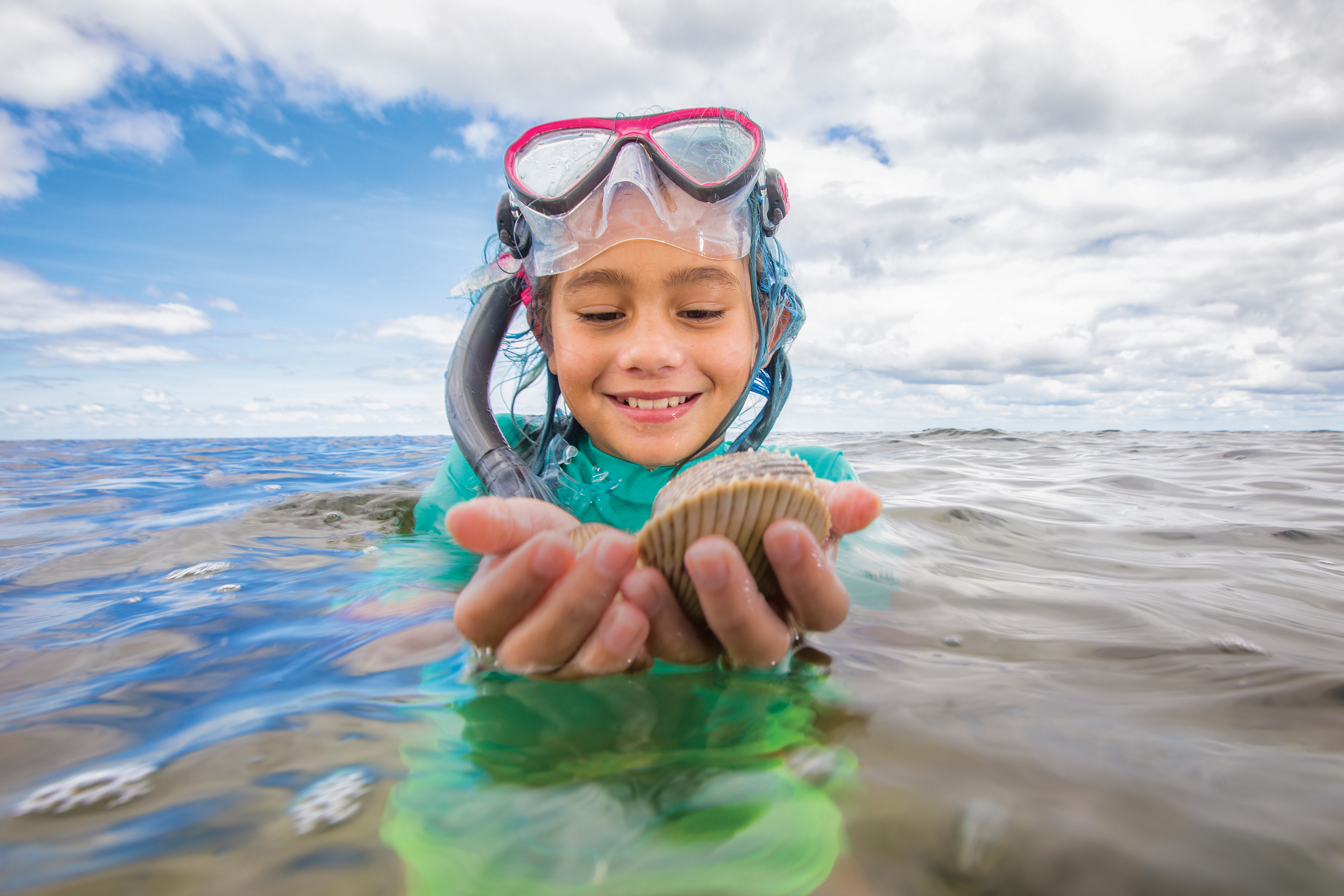 Child holds shells in hand while standing in the ocean waters.