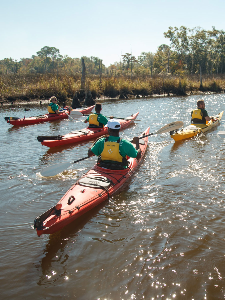 Team of conservationists in kayaks floating along the Mississippi coastline as they conduct work in the field.