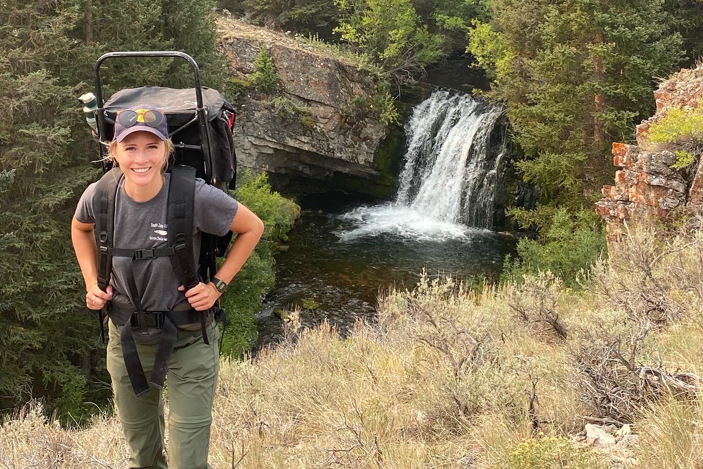 Young woman with a backpack and a waterfall in the background.