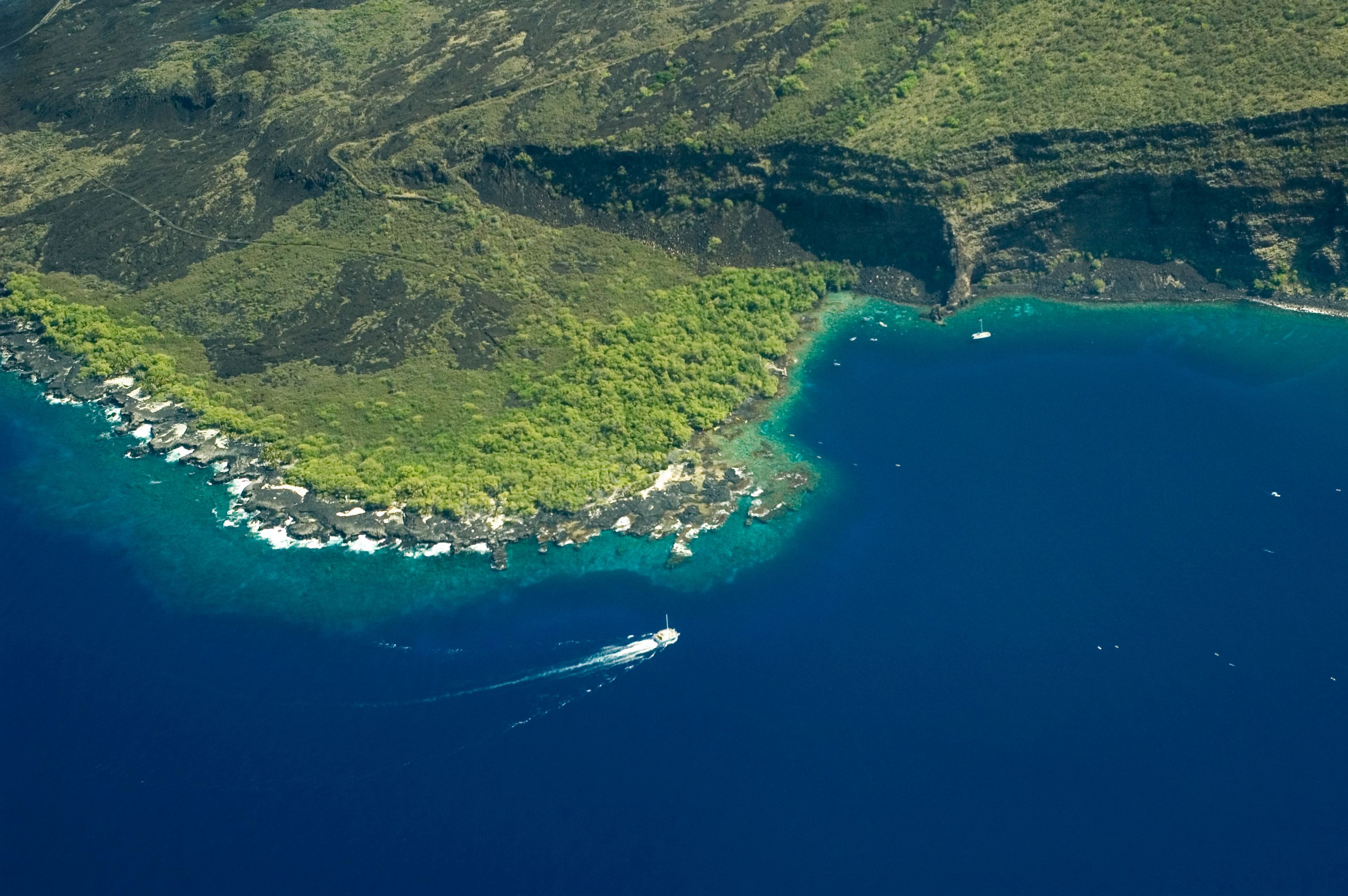Tour boat travels along rocky shoreline to enter the bay, with undeveloped coastal area and cliffs in the background.