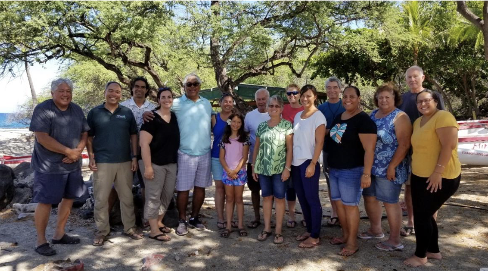 Kai Kuleana members and Kealakekua leaders standing in the sand near the shore, with vegetation in background.