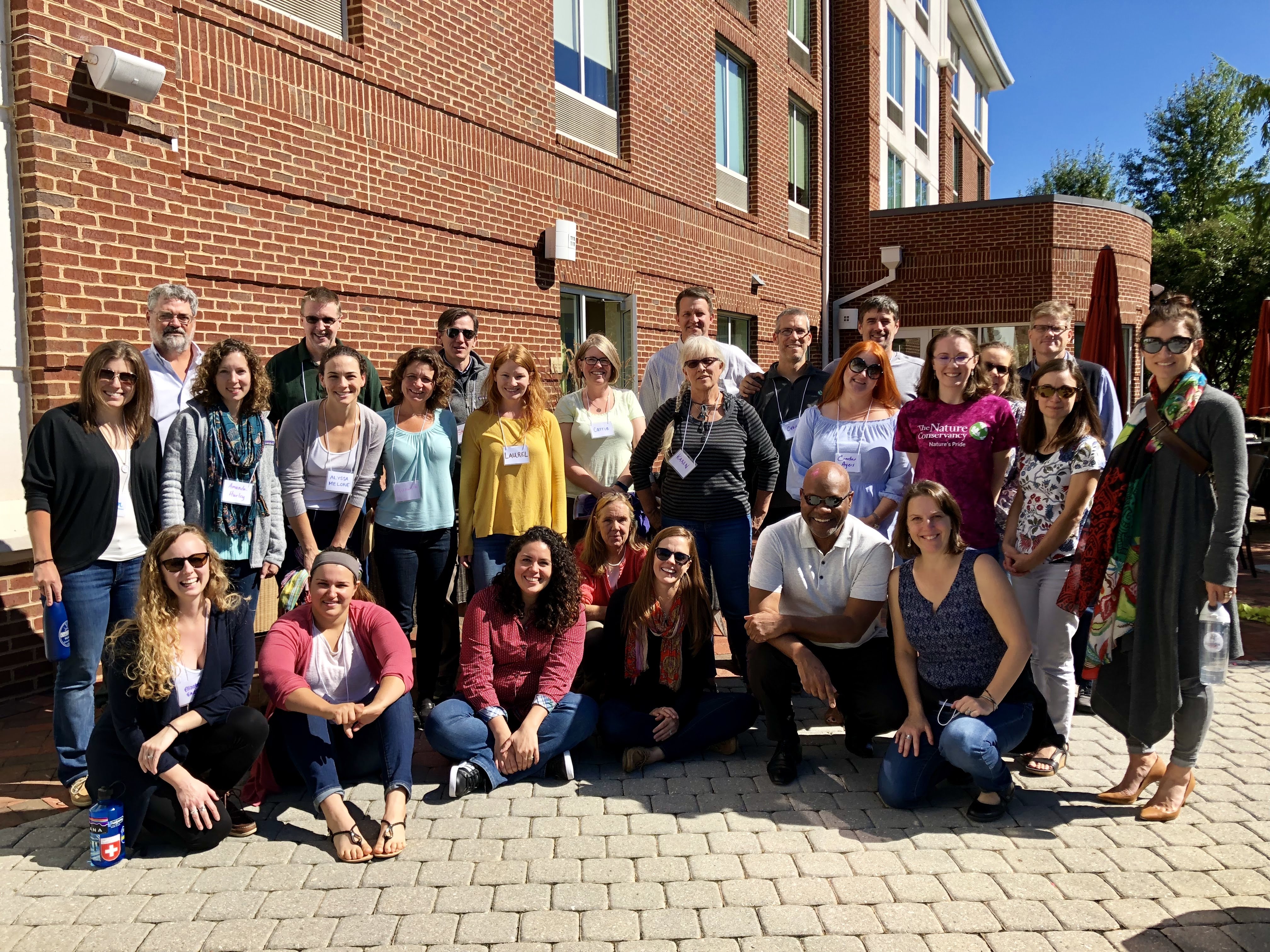 Group of people pictured in front of a brick building on a sunny day.