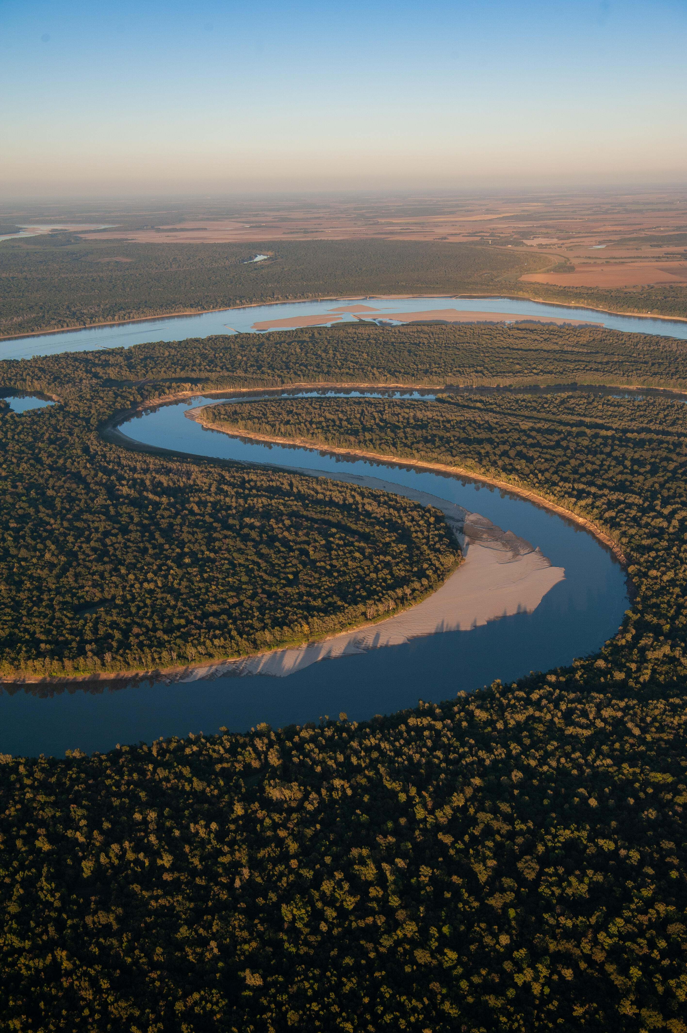 Aerial view of a winding Mississippi River cutting through a thickly forested landscape.