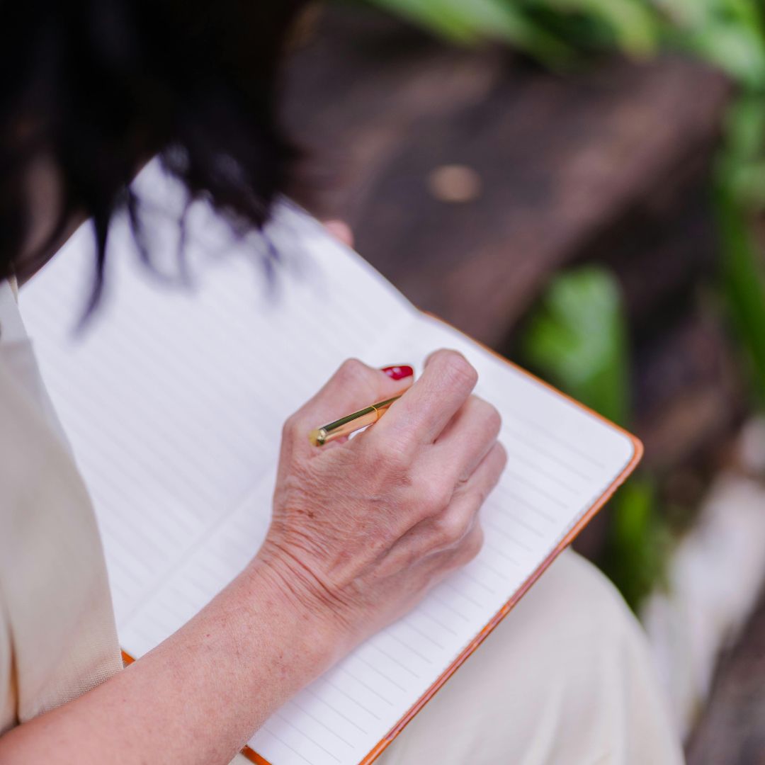 A person holding a pen over an open lined journal in their lap. 