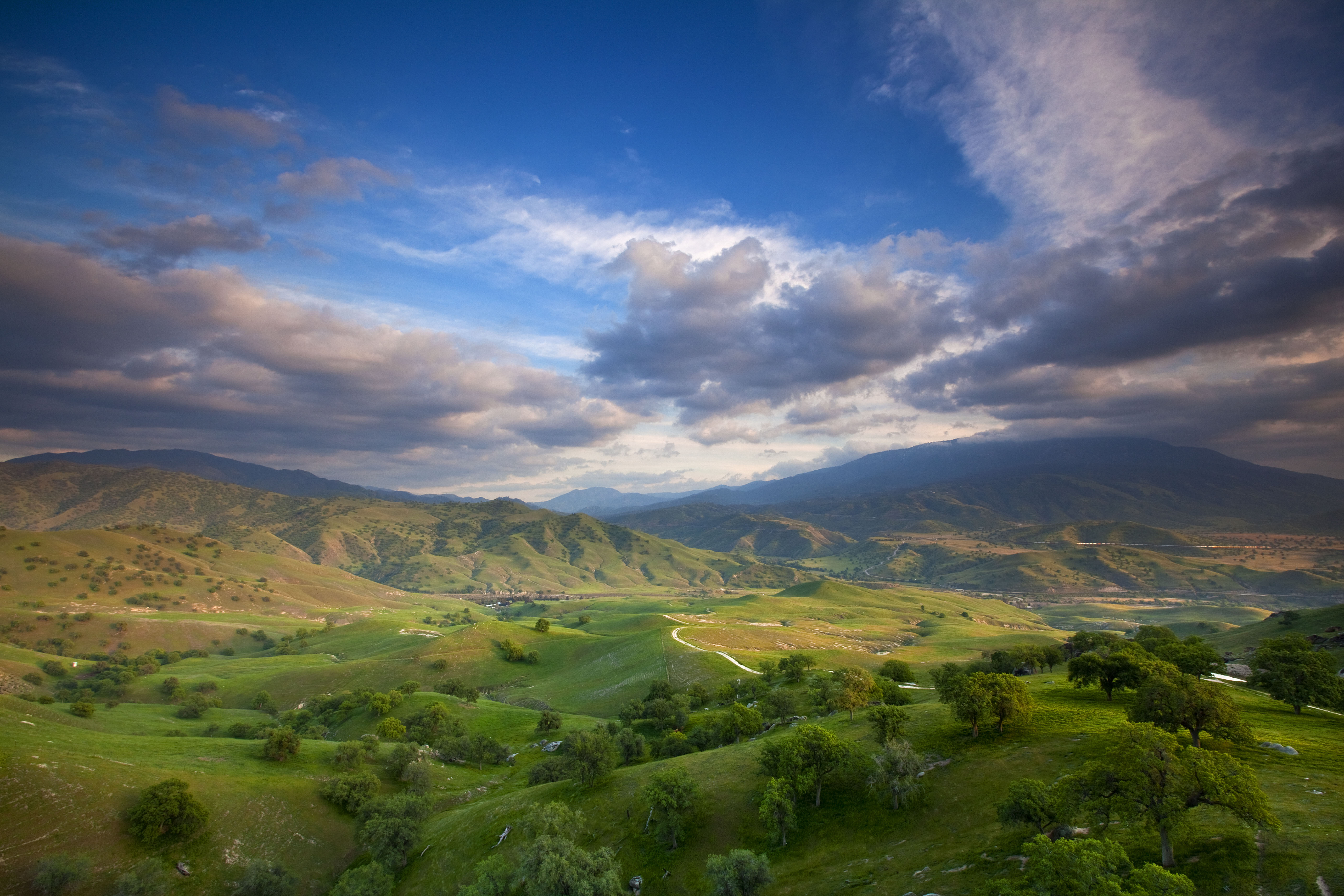 View looking across a wide valley with rolling green hills and mountains in the distance.