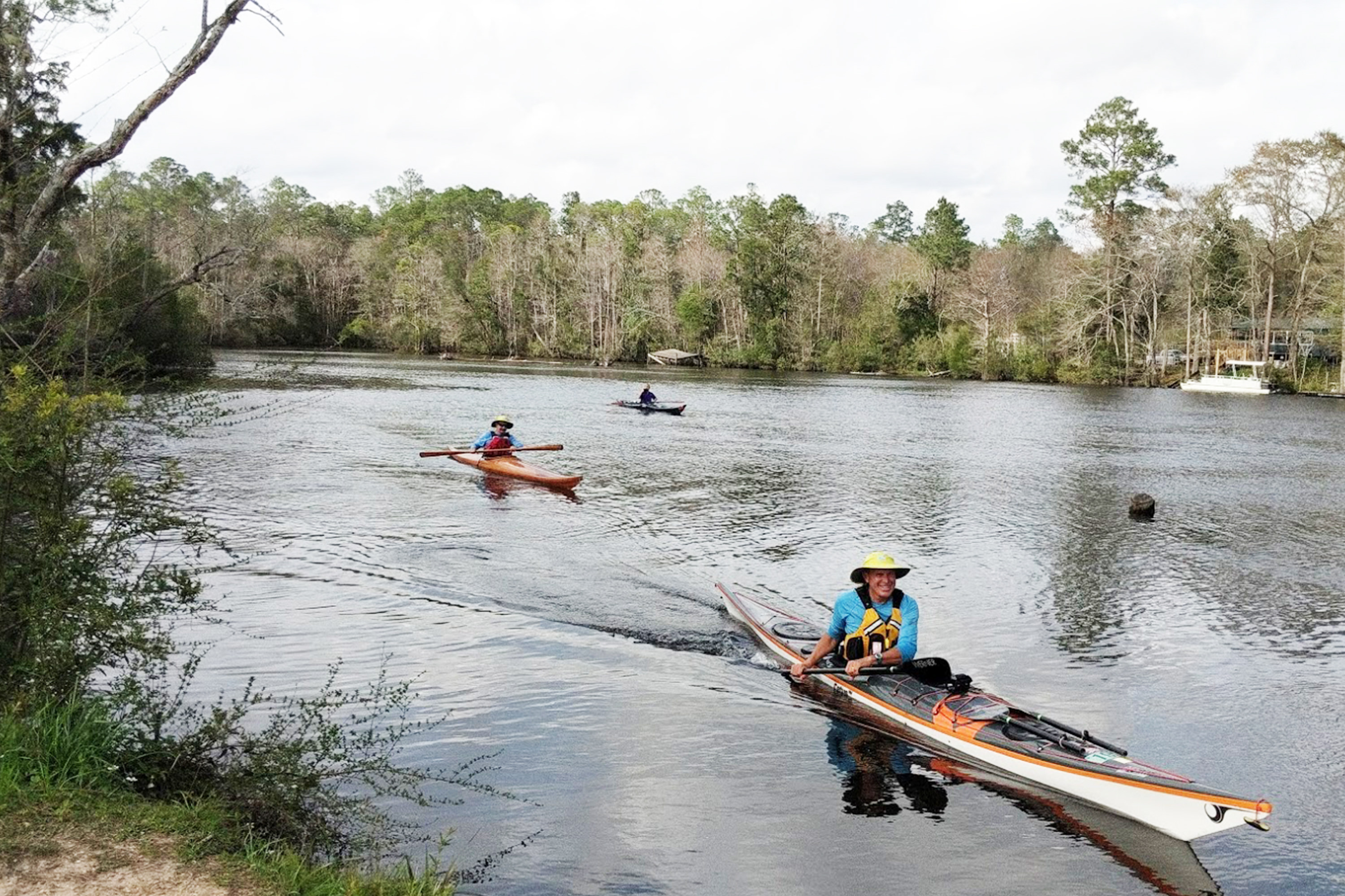 Three men in kayaks enjoy paddling and kayaking on the wide Perdido River in Florida.