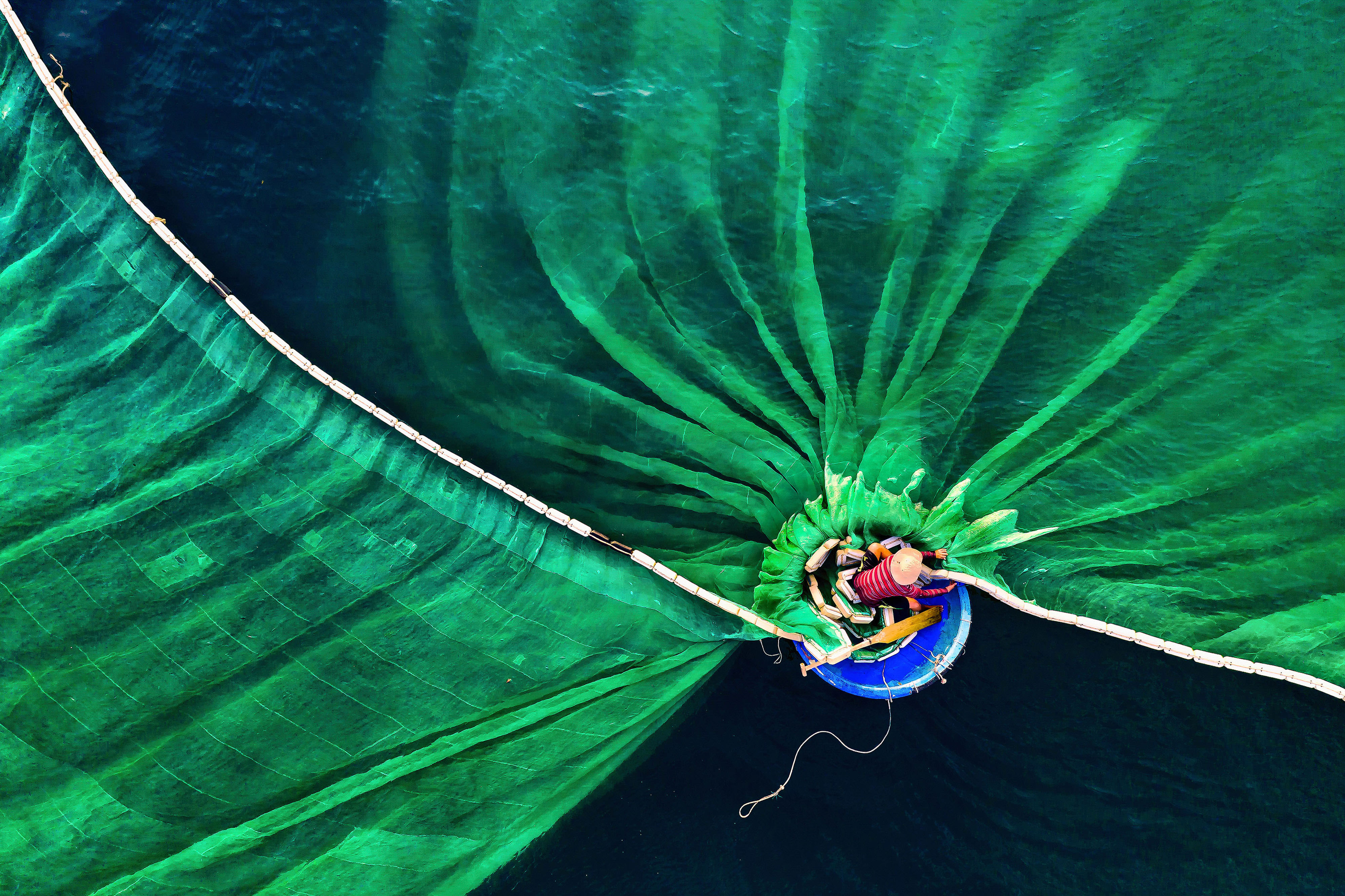 Overhead view of a man on a boat casting a wide, green net.