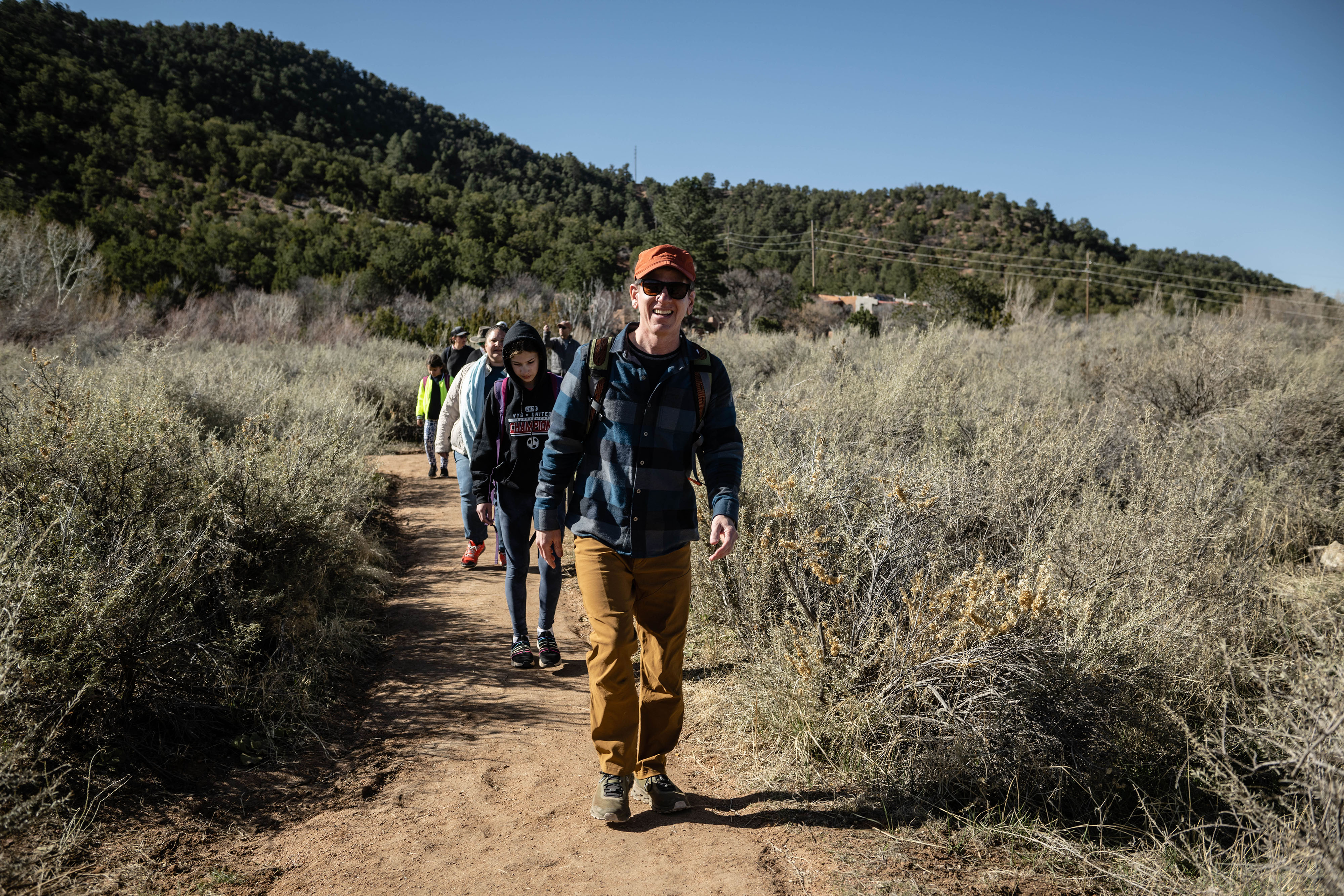 A line of people hike on a dirt trail in the desert.
