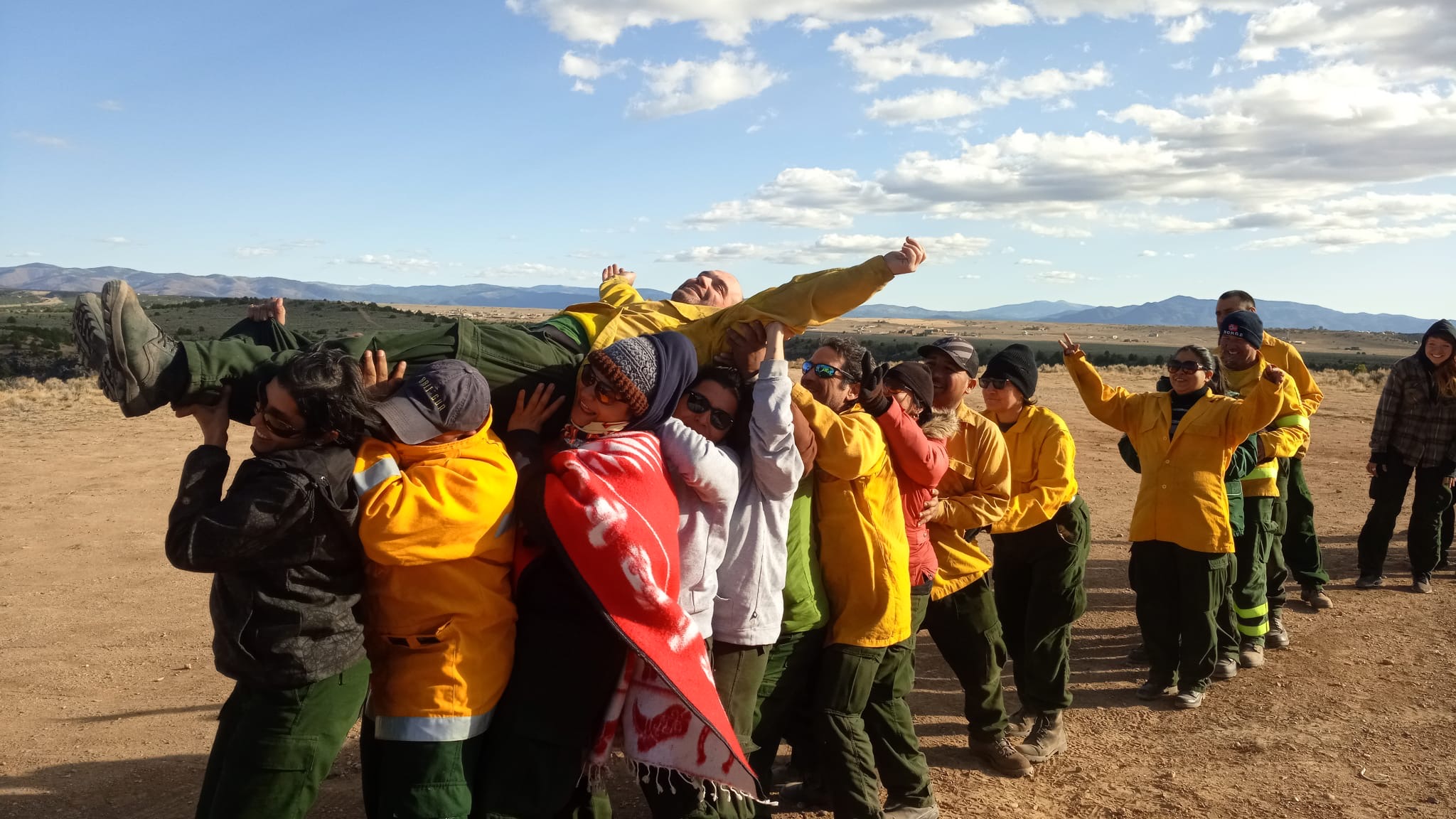 A dozen wildland fire workers engage in a trust-building exercise by carrying a man over their heads.