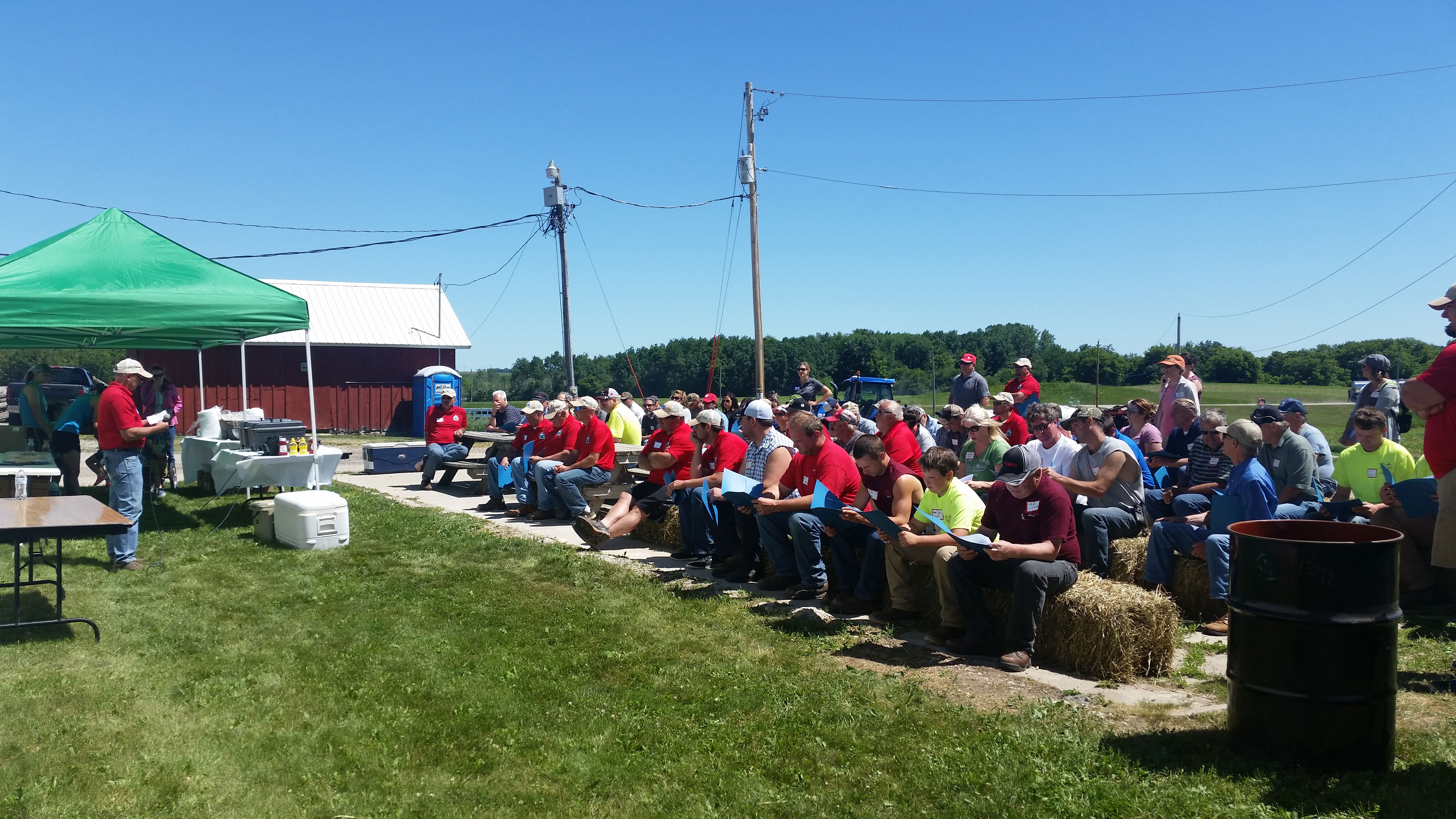Man speaking to large group of farmers in front of farm field.