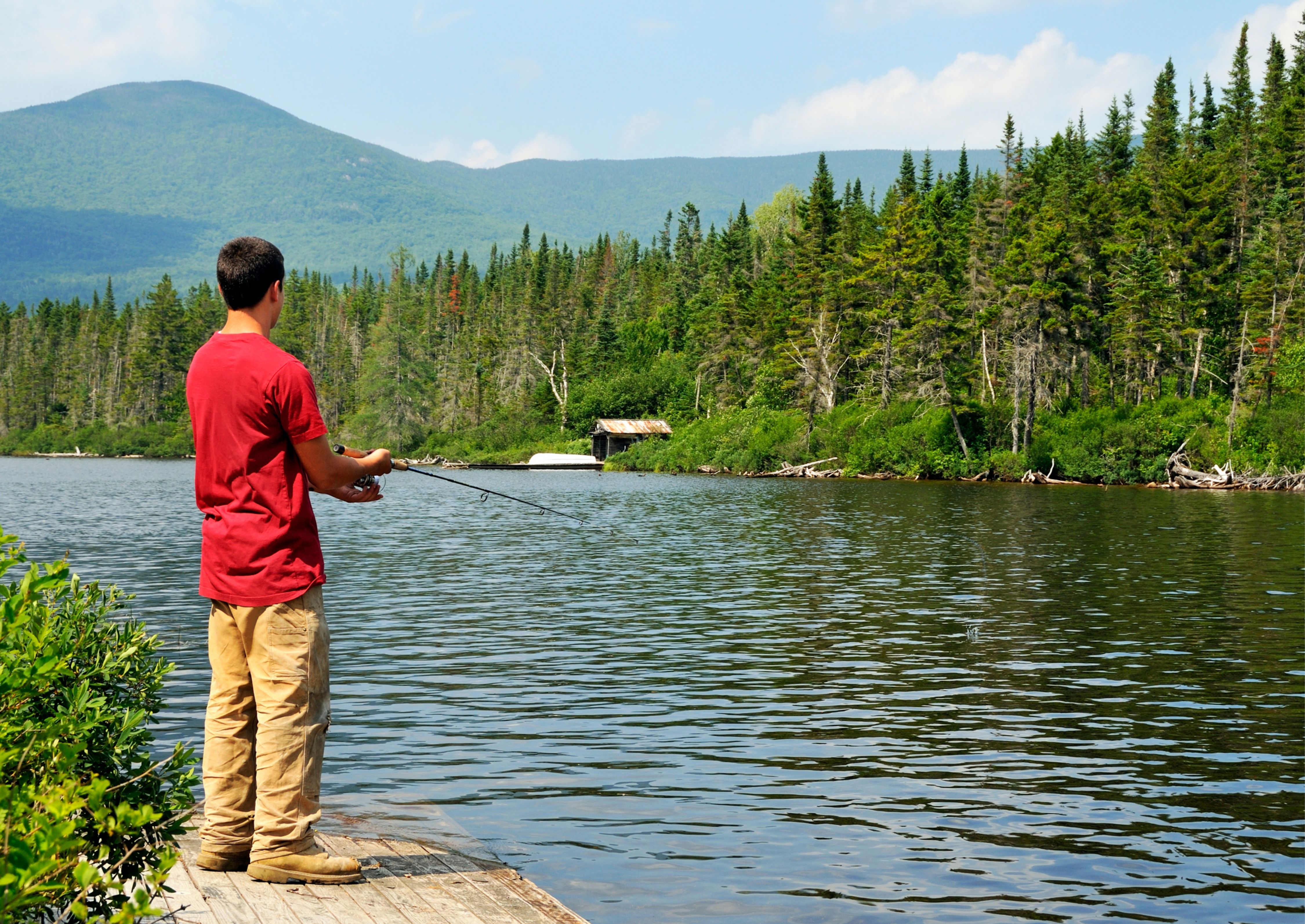 A man in a red shirt fishing in a lake.