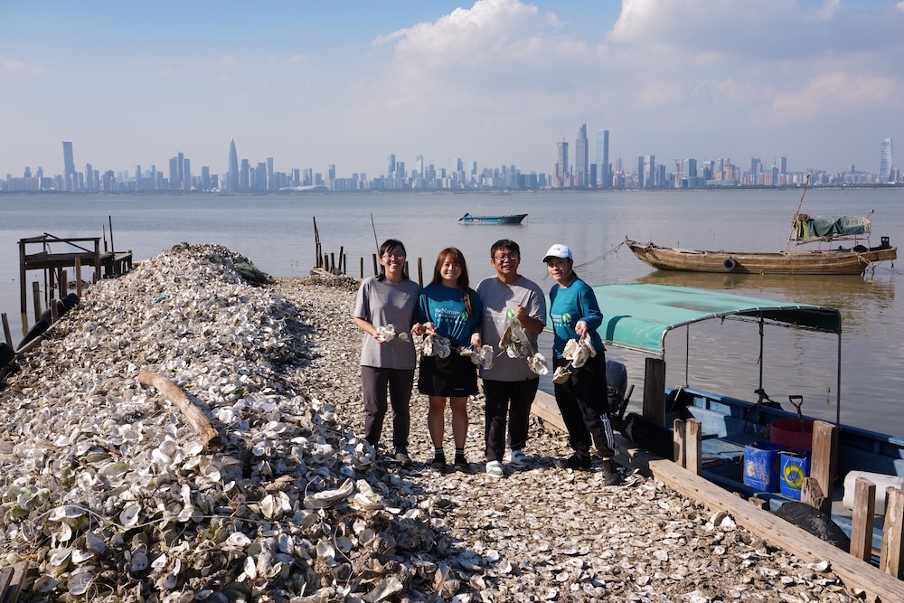 Four people holding shellfish shells on a broadwalk.