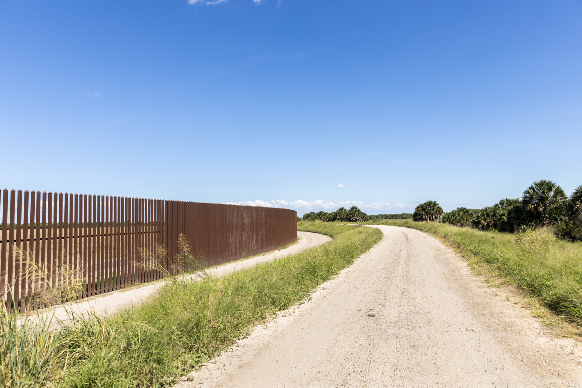 A wall runs along the length of a gravel road.