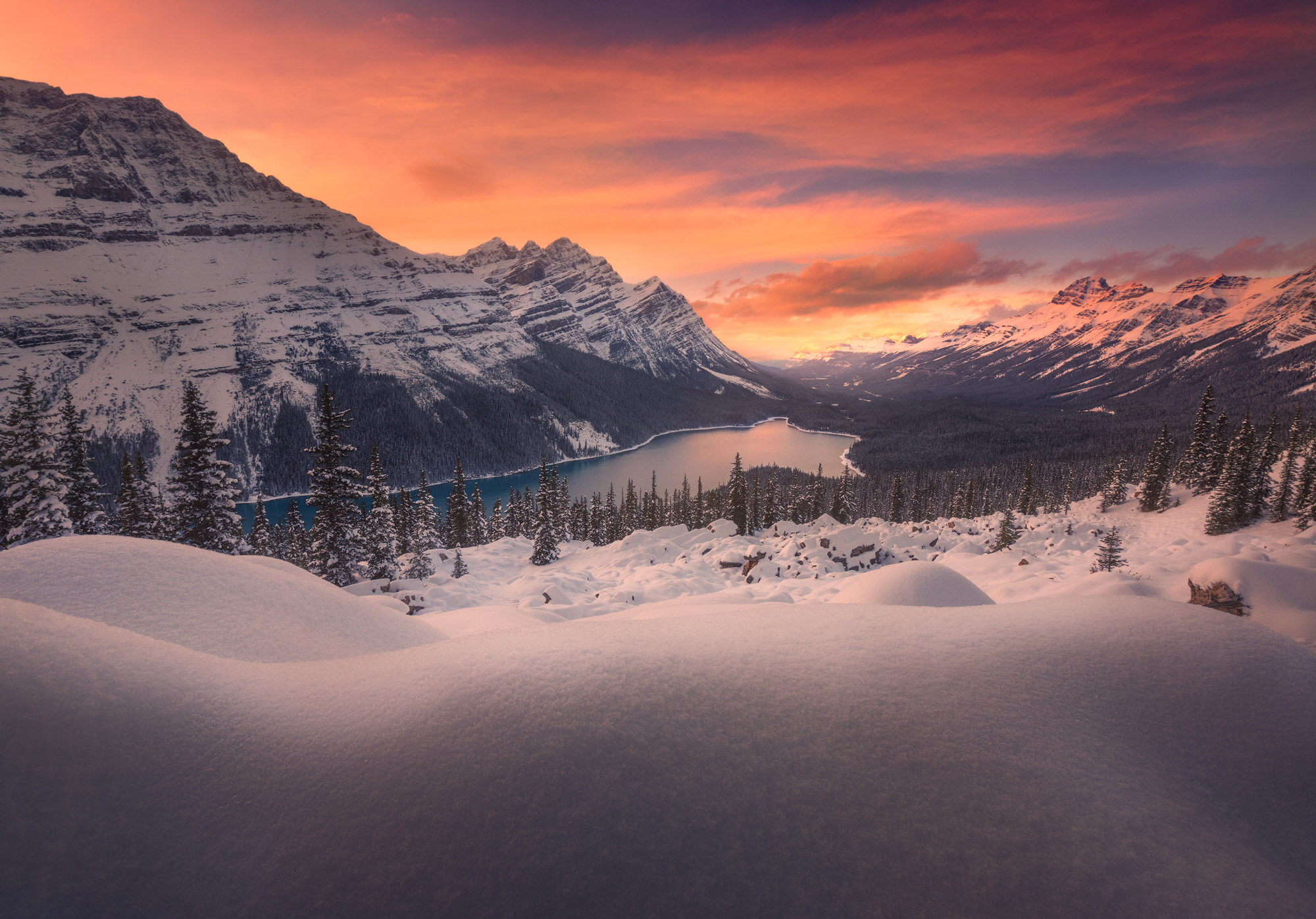 Glowing clouds illuminate snowy mountain lake.