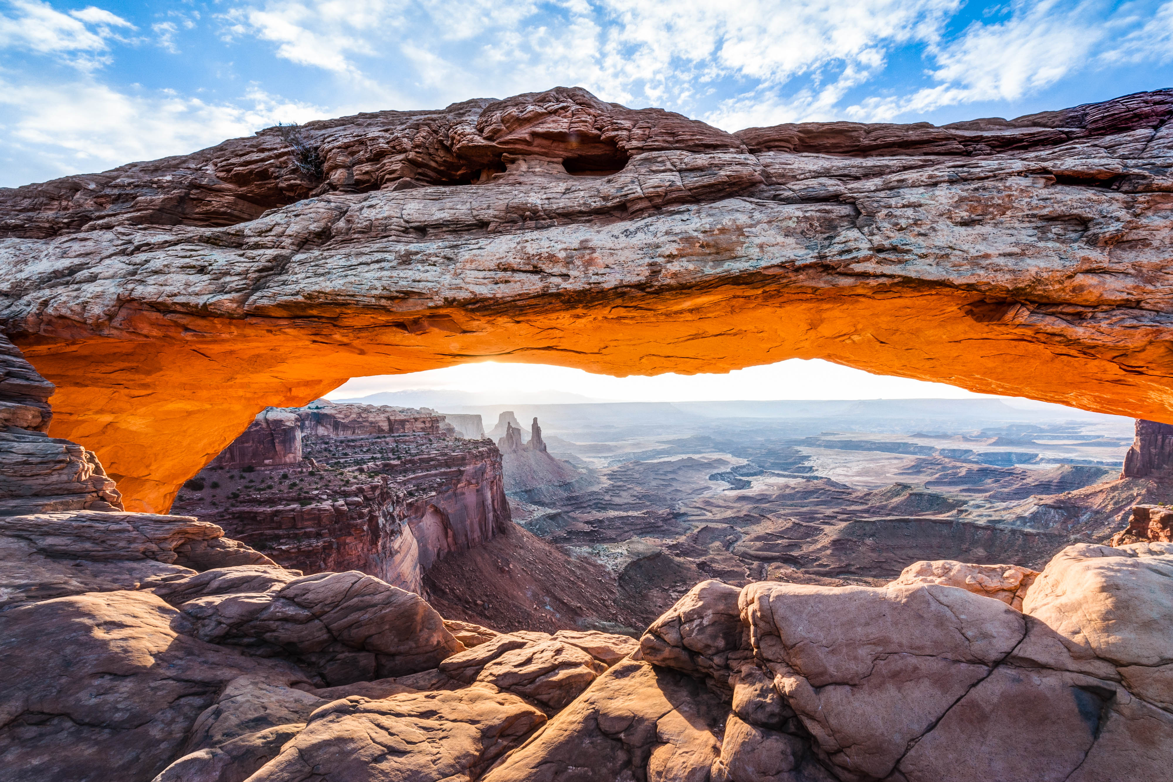 A large stone arch extends in the foreground over a desert landscape in the distance.