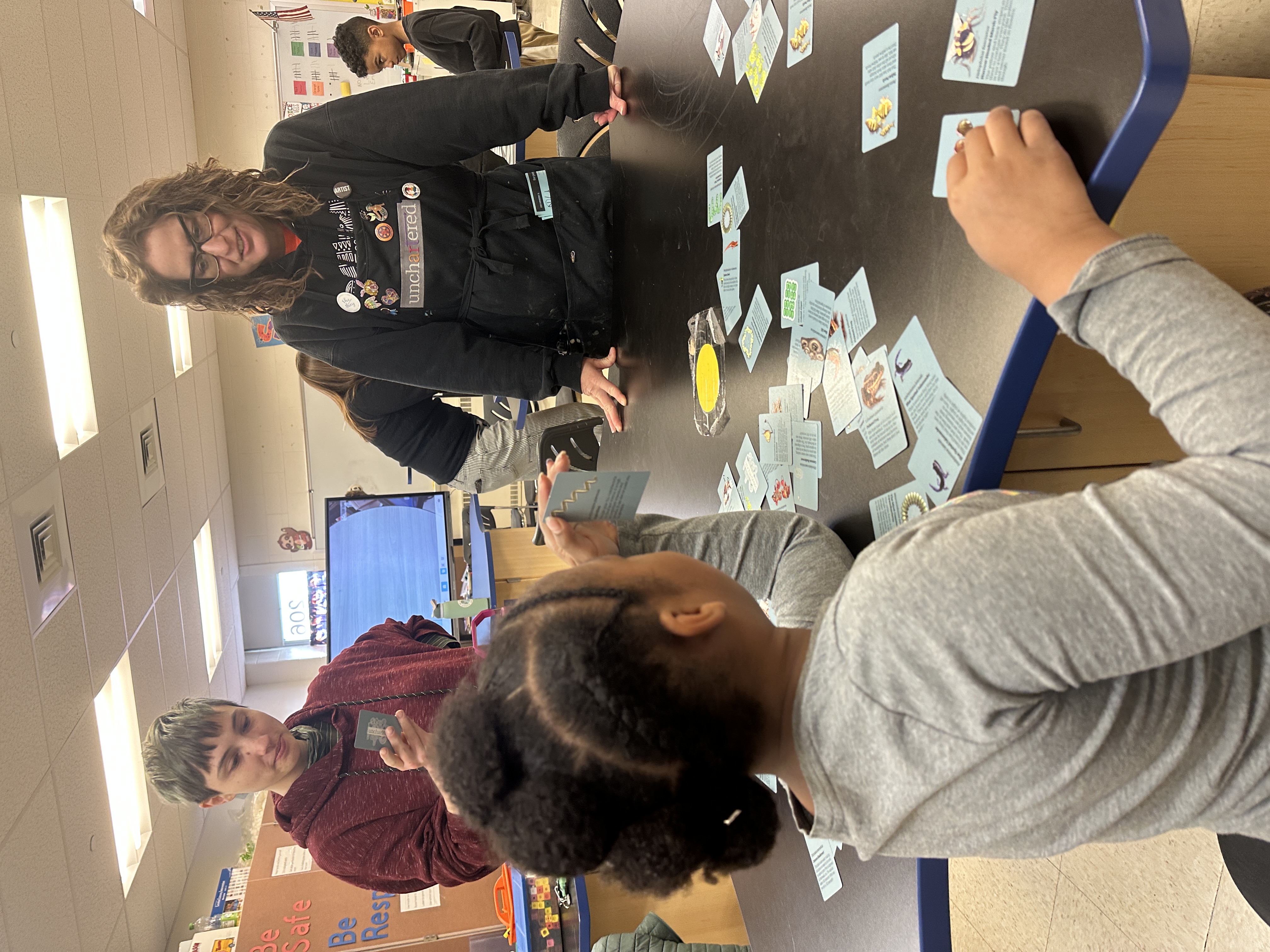Children playing a card game while the teacher looks on.
