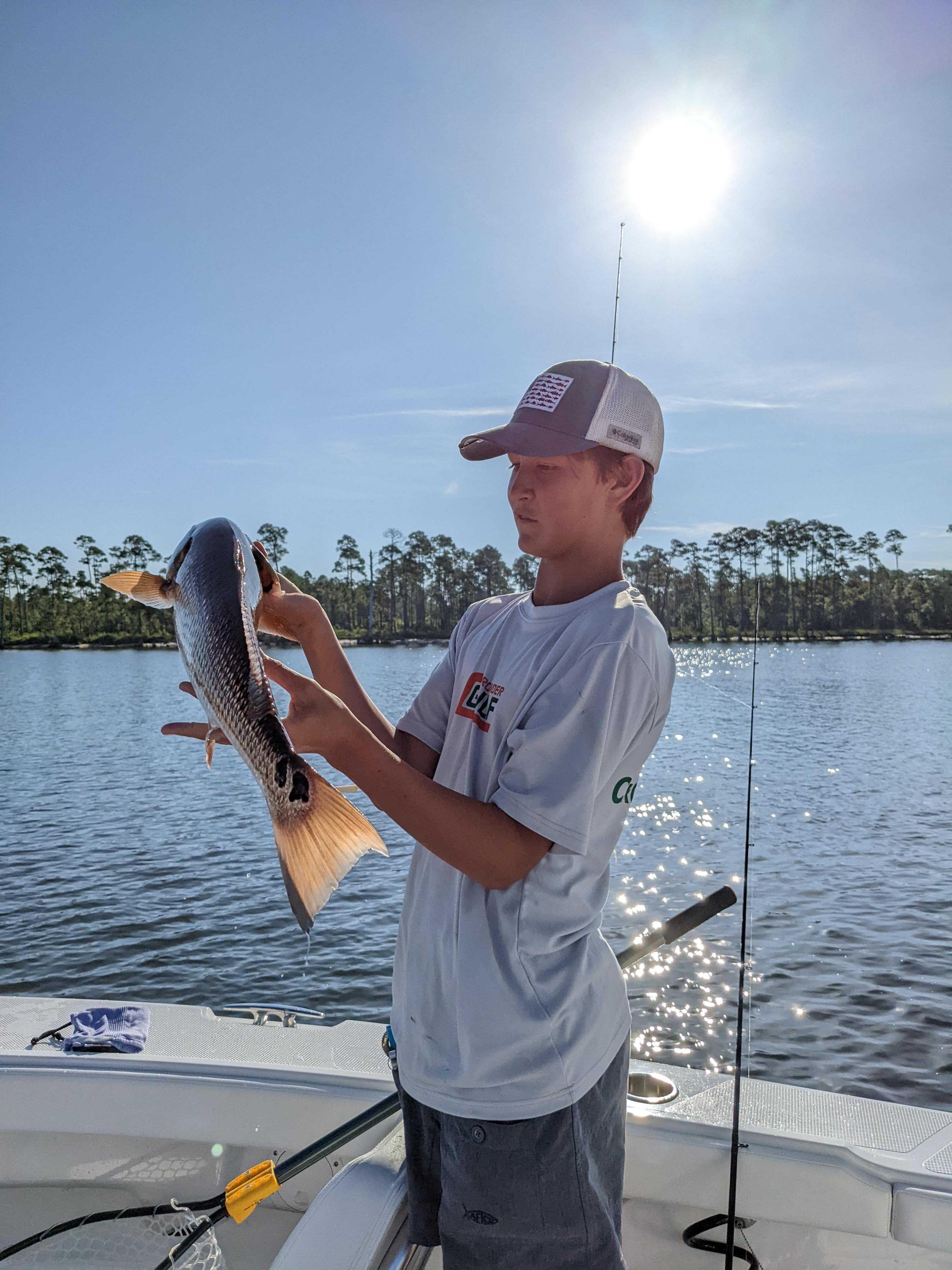 Boy holding a fish on a boat.